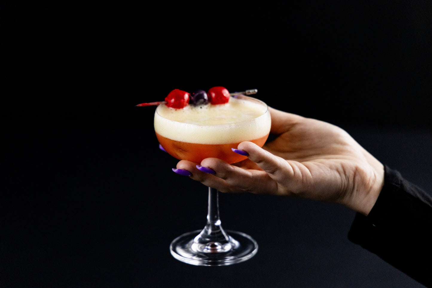 Hand holding a craft cocktail garnished with cherries, topped with a thick layer of foam, emphasizing CloudTails revolutionary mouthfeel that transform the cocktail into a visually stunning, craft-quality drink.